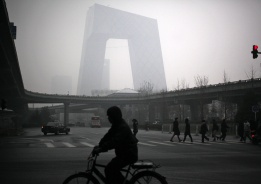 Пешеходци и колоездачи пред сградата на Централната китайска телевизия, потънала в мъгла, Пекин, Китай, 5 декември.