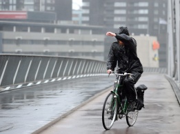 Колоездач прикрива лицето си от силния вятър и дъжд, докато се движи по една от улиците на Ротердам, Холандия.