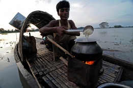 Рибар приготвя вечеря в лодката си преди нощния риболов в наводнената провинция Маригаон в Североизточна Индия.