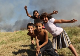 Деца от ромската махала в кв. Орландовци в София позират на фона на разразилия се на мястото пожар.