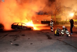Шведски пожарникари гасят горяща кола в предградието Киста, Стокхолм, където за трета поредна нощ младежи създават размирици, палейки коли и замеряйки полицията с камъни. Смята се, че бунтовете са причинени от полицейска акция в предградието Хъсби, в коят