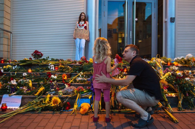 Баща и дъщеря поставят цветя в памет на загиналите жертви от катастрофиралия в Украйна боинг, пред момиче с надпис "Путин убиец" пред посолството на Холандия в Киев