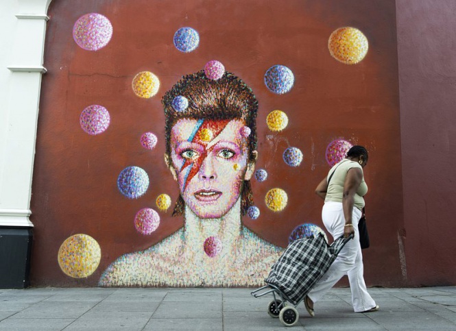 Жена минава покрай стенопис, изобразяващ британския музикант Дейвид Бауи в Южен Лондон, Великобритания.